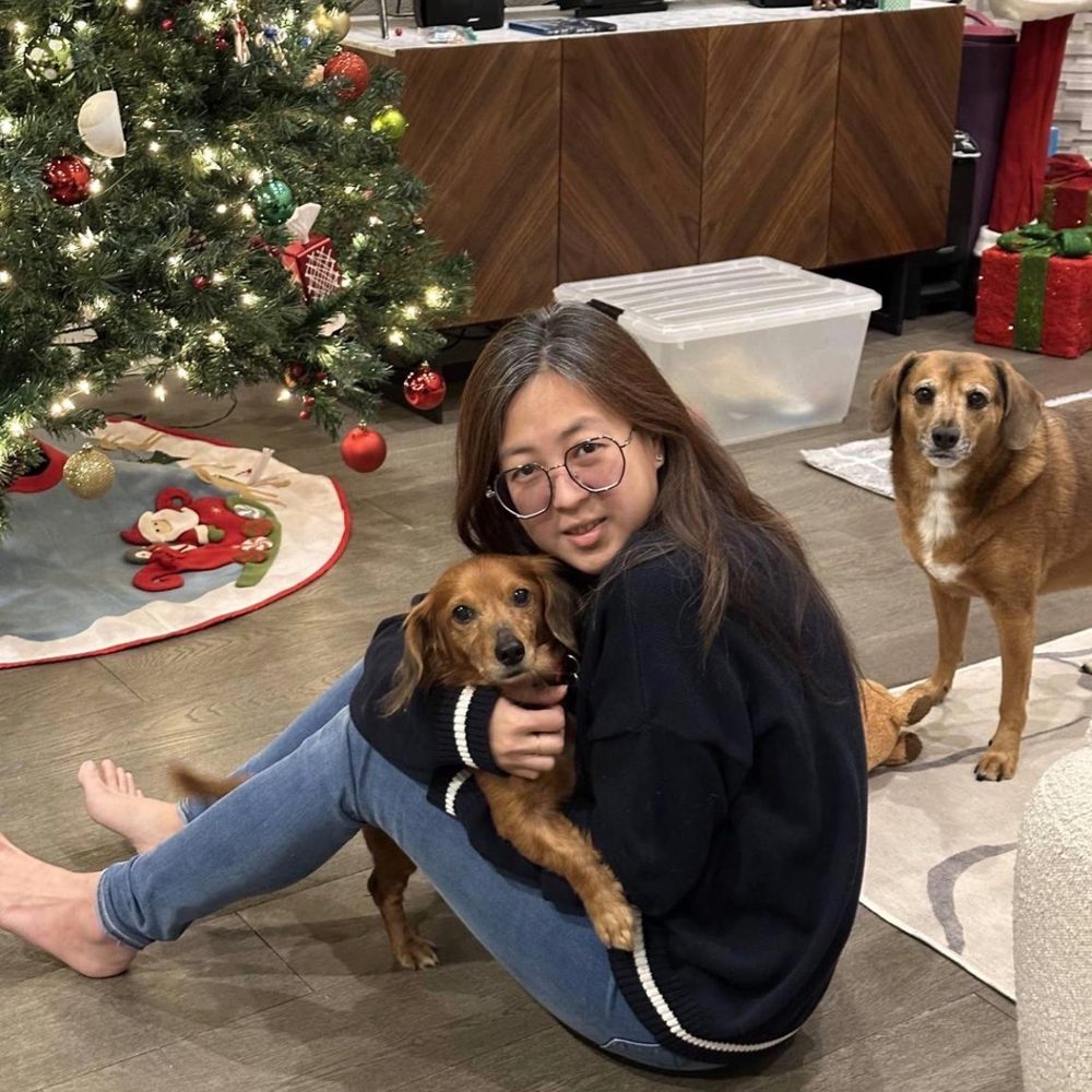 Christine sitting on the floor hugging a small brown dachshund, with another dog standing nearby